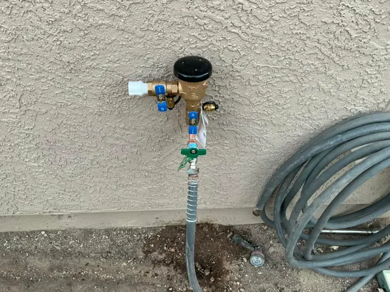 Outdoor hose bib with a pressure regulator and backflow device on a stucco wall.