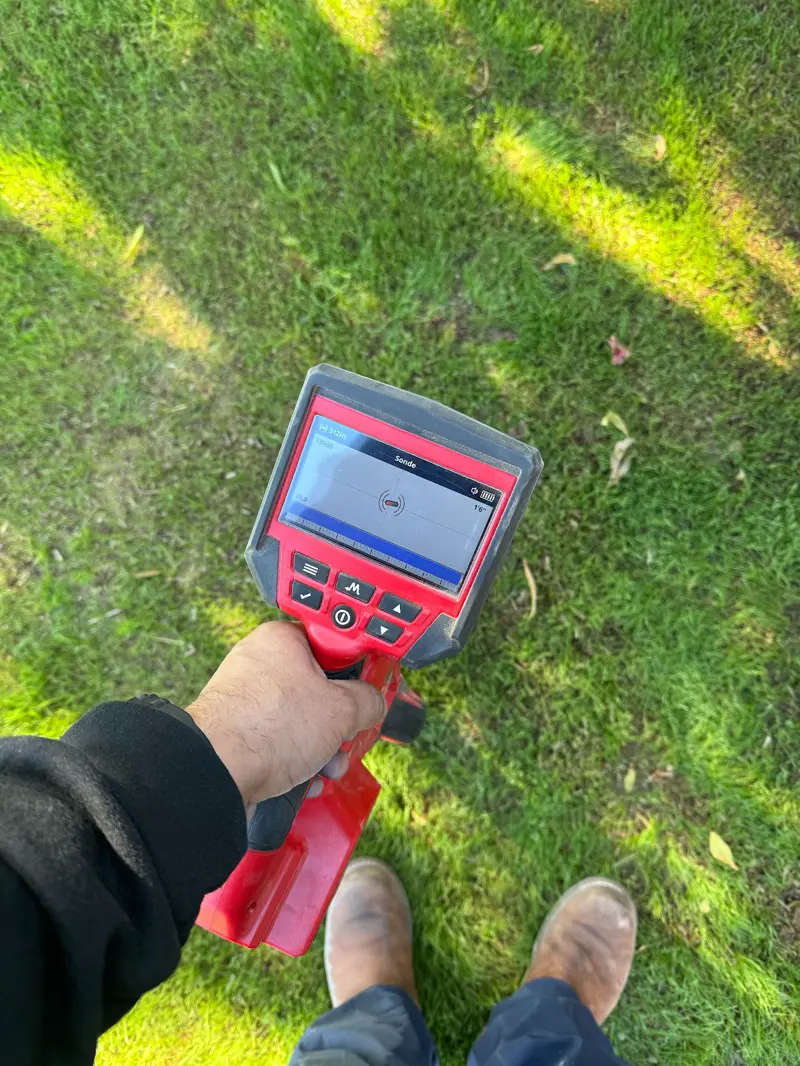 Technician using a sewer line locator over a front lawn to trace the pipe from above.