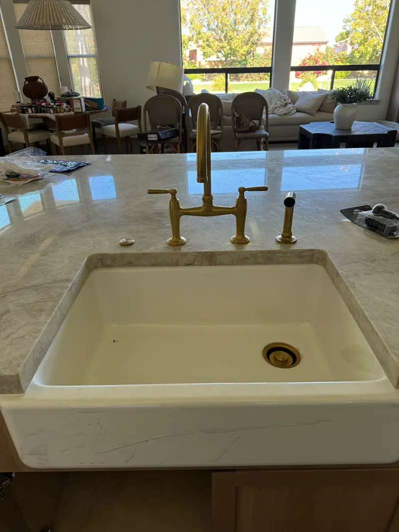 Farmhouse sink with a newly installed brass bridge faucet.
