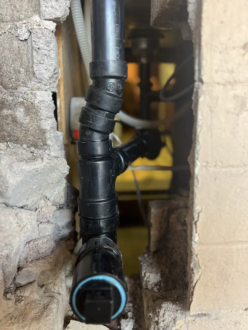 ABS drain stack exposed in a block wall during drain line work.