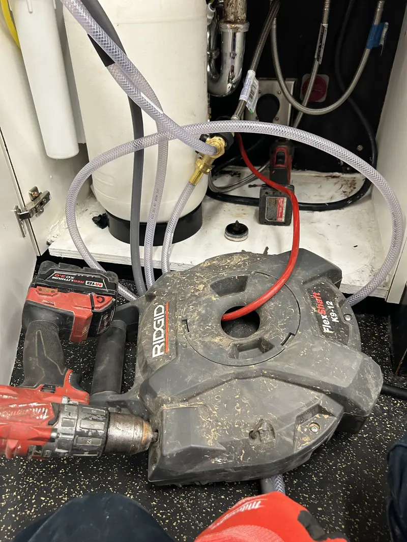 Drain cleaning machine set up under a kitchen sink.