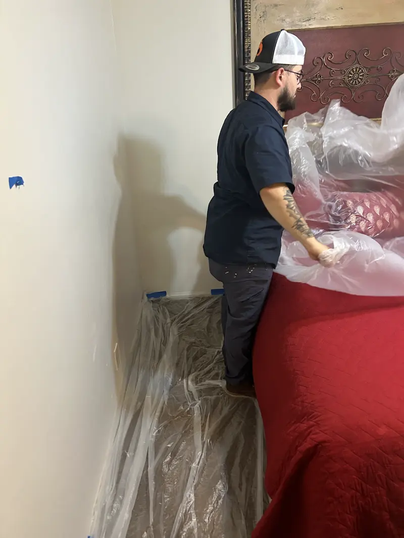 Technician covering a bed with plastic to protect the home before plumbing work.