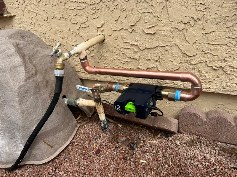 Smart water shutoff valve installed on an exterior copper water line for leak protection.