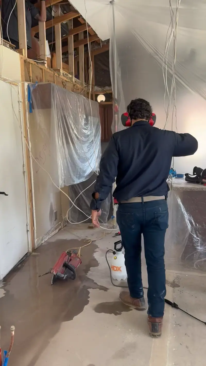 Technician in a water-damaged room with plastic containment set up after a leak.