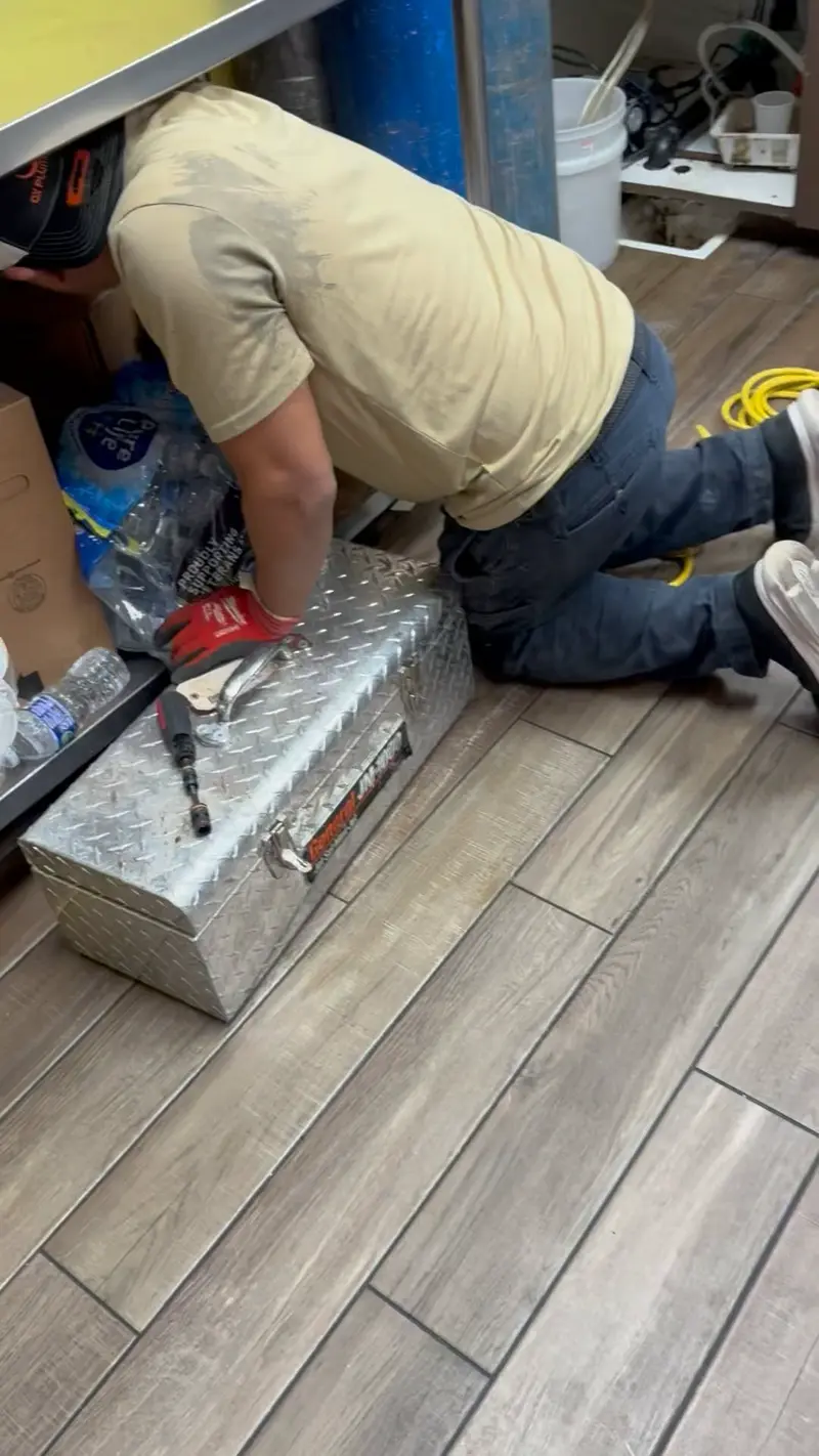 Technician kneeling under a sink with a toolbox.